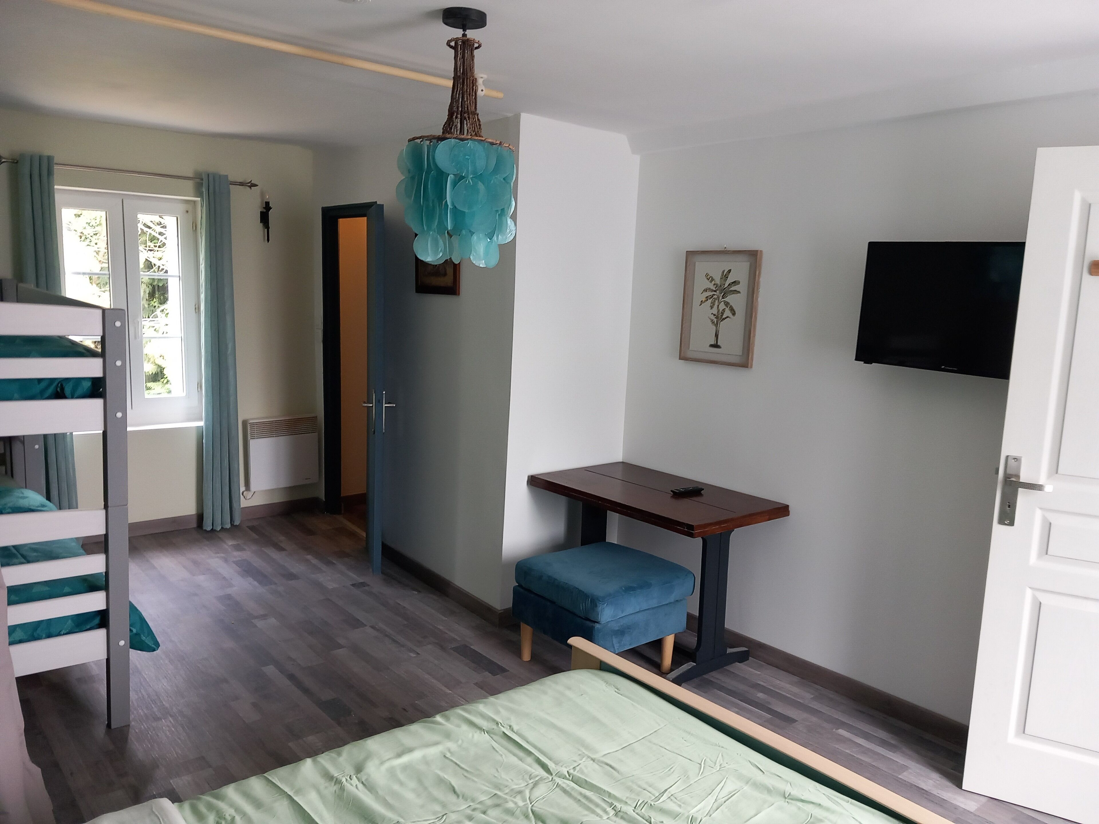 A room with a bunk bed, a desk with a chair, a television, and a door.