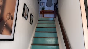 A staircase with teal steps and a wooden handrail, leading to a landing with a plant and framed artwork. - 3 BEDROOMS Villedieu les poeles MONT SAINT MICHEL (Sainte-Cécile)