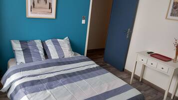 Cama bem arrumada com colcha estampada, mesa de cabeceira com bandeja vermelha e quadro na parede.