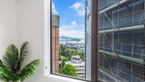 A room with a large window offering a view of a cityscape, including buildings and a bridge. - Central 3BR Full Kitchen & Amenities Zodiak Stays (Auckland)