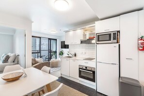 A modern kitchen with white cabinetry, a built-in oven, a microwave, and a stainless steel refrigerator. - Central 3BR w/ Full Kitchen & Amenities by Zodiak (Auckland)