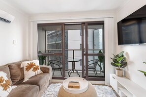 A modern living room with a sofa, a coffee table, and a balcony with chairs. - Central 3BR w/ Full Kitchen & Amenities by Zodiak (Auckland)