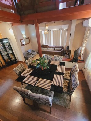 Un espace repas avec une table centrale entourée de chaises à motifs, un canapé en arrière-plan et un grand miroir au mur.