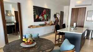 Eine moderne Küche mit Kochinsel, ein Essbereich mit rundem Tisch und blauen Stühlen sowie ein großes Bild an der Wand.