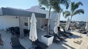 Eine Dachterrasse mit Liegestühlen, Sonnenschirmen und einem Essbereich.