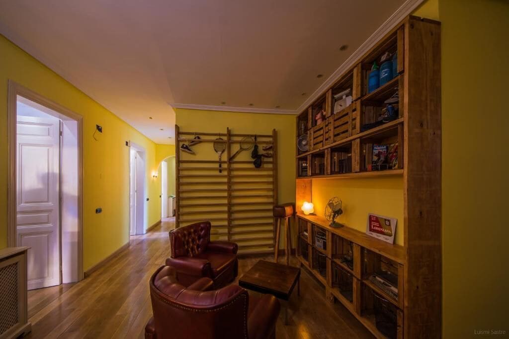 A hallway with a wooden chair, a small table, and a bookshelf filled with books and items.