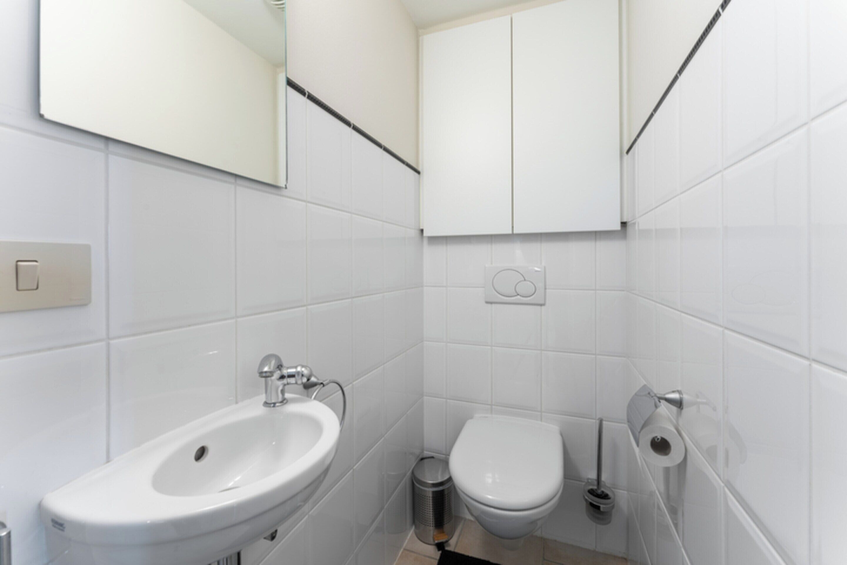 Ein modernes Badezimmer mit Waschbecken, Toilette und Spiegel, alles in Weiß.