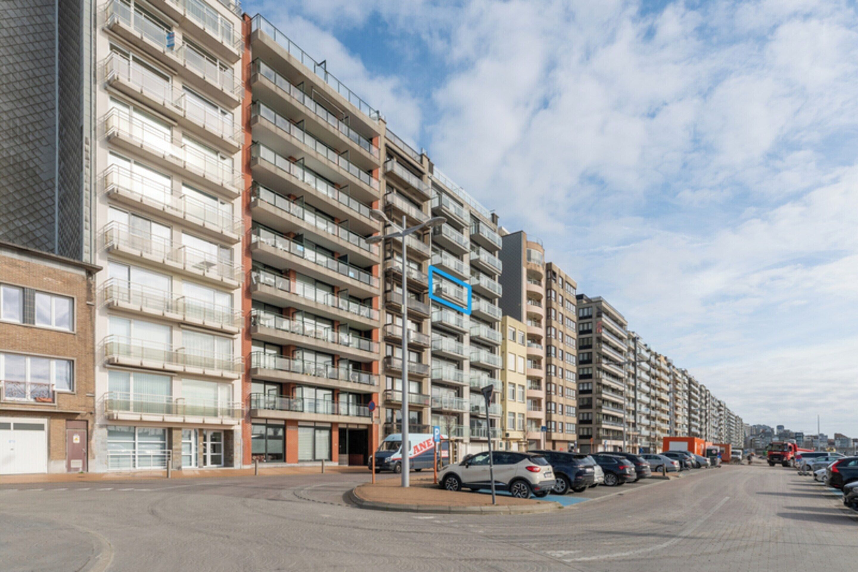 Ein mehrstöckiges Wohngebäude mit Balkonen, einem Parkplatz und blauem Himmel.