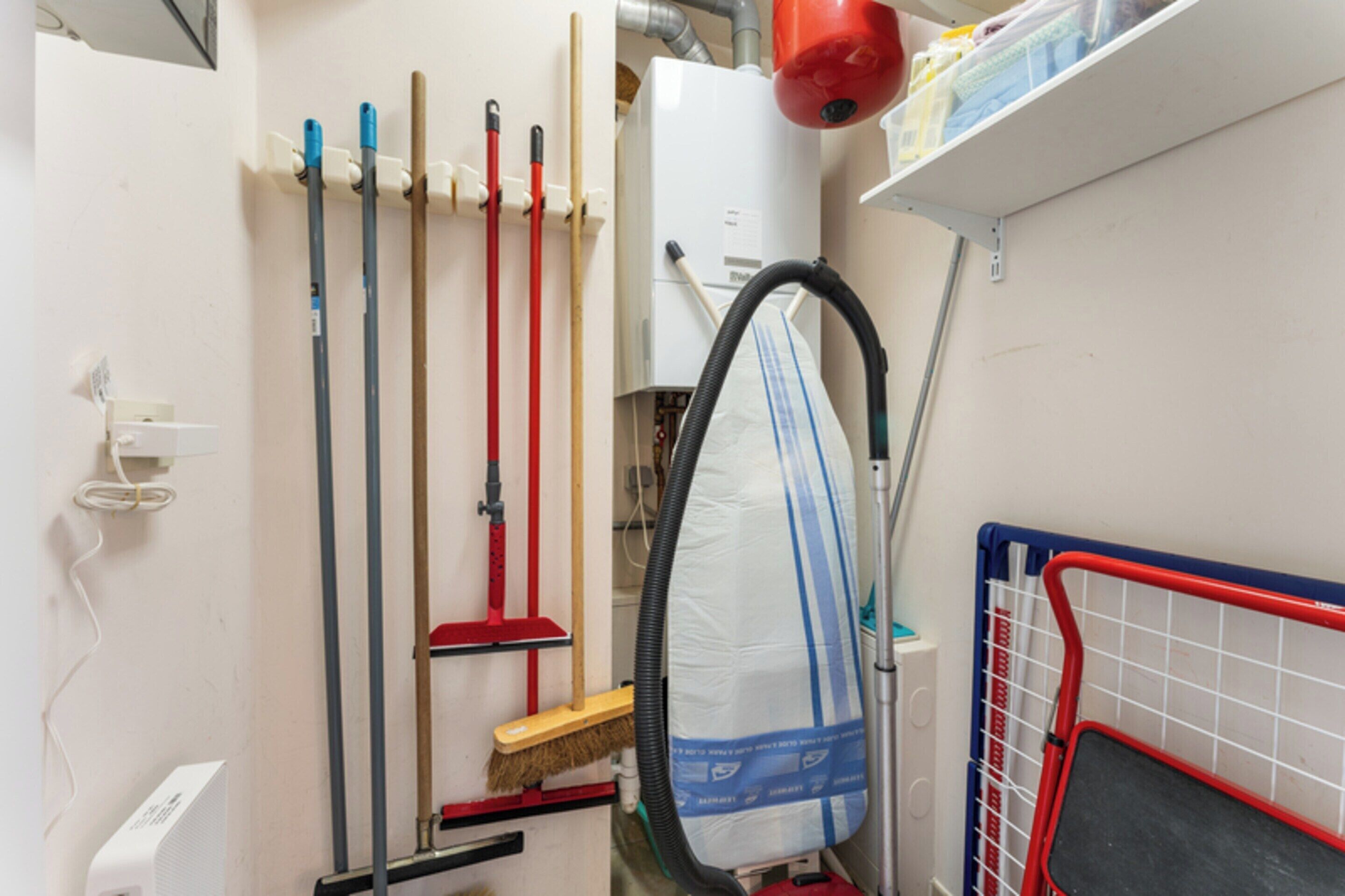 A utility room with cleaning equipment, a vacuum cleaner, and a storage rack.