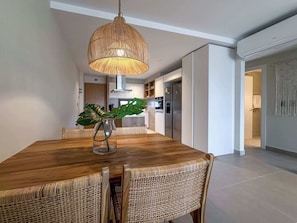 Een moderne eethoek met een houten tafel, rieten stoelen en een hanglamp.