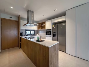 Een moderne keuken met een centraal eiland, roestvrijstalen apparatuur en een houten deur.