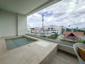 Een balkon met een zwembad, een stoel en uitzicht op een woongebied met gebouwen en een hoge zendmast.