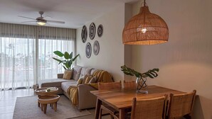 Una sala de estar moderna con comedor, que incluye un ventanal grande, un ventilador de techo y una mesa de comedor con sillas de mimbre.
