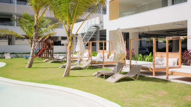 A modern outdoor lounge area with sun loungers, a children's play structure, and a pool.