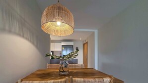 A dining area with a wooden table and four wicker chairs, a hanging wicker lamp, and a vase with a plant.