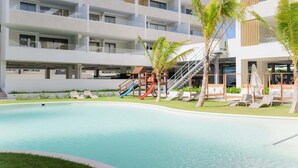 A modern hotel with a swimming pool, a children's play area, and lounge chairs.
