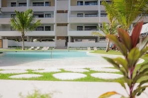 Ein modernes Hotel mit Pool, Palmen und Liegestühlen.