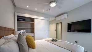 A modern hotel room with a large bed, built-in storage, a flat-screen TV, and an air conditioning unit.