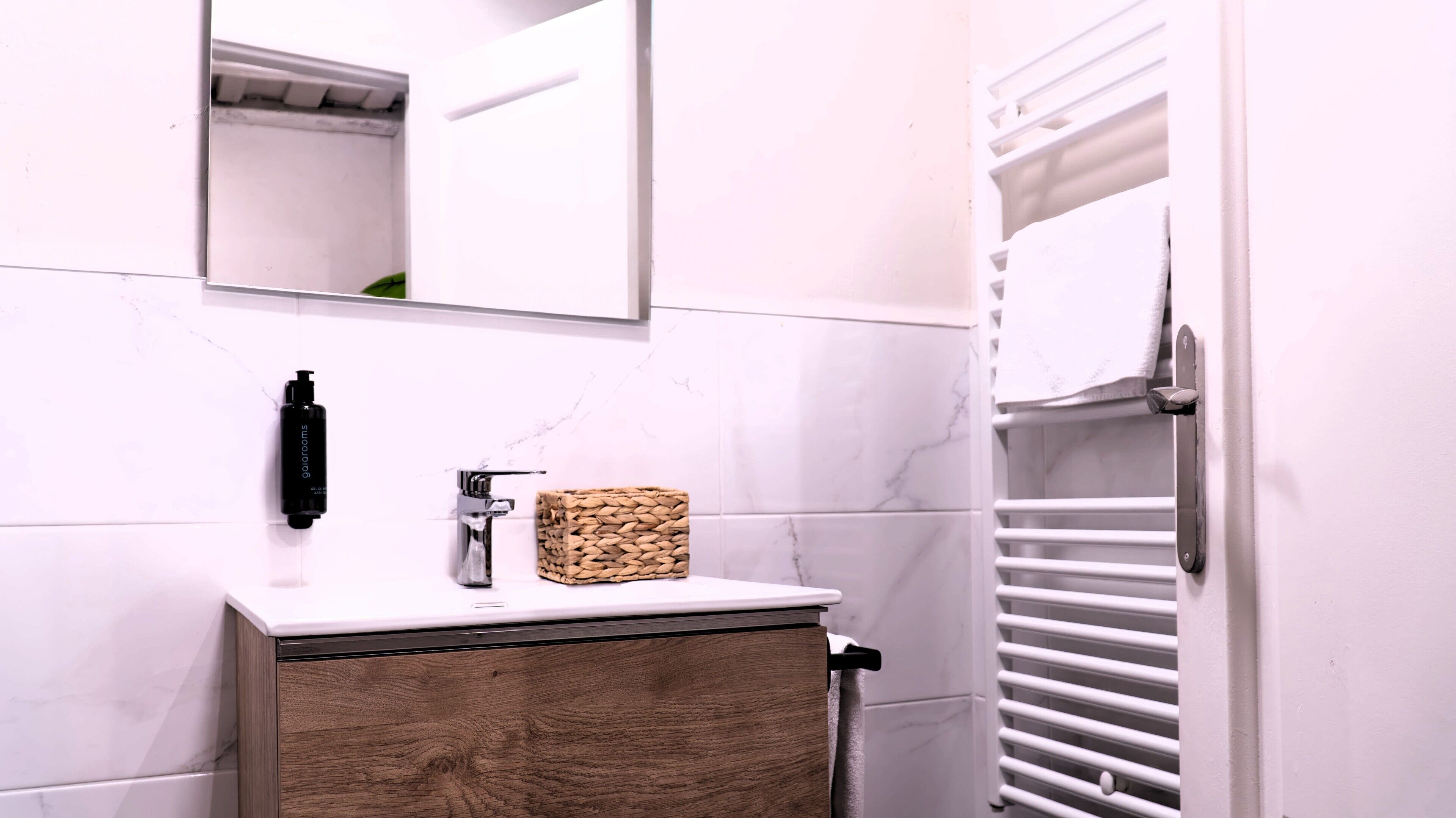 A bathroom with a marble-tiled wall, a wooden cabinet, a mirror, a towel rack, and a white door.