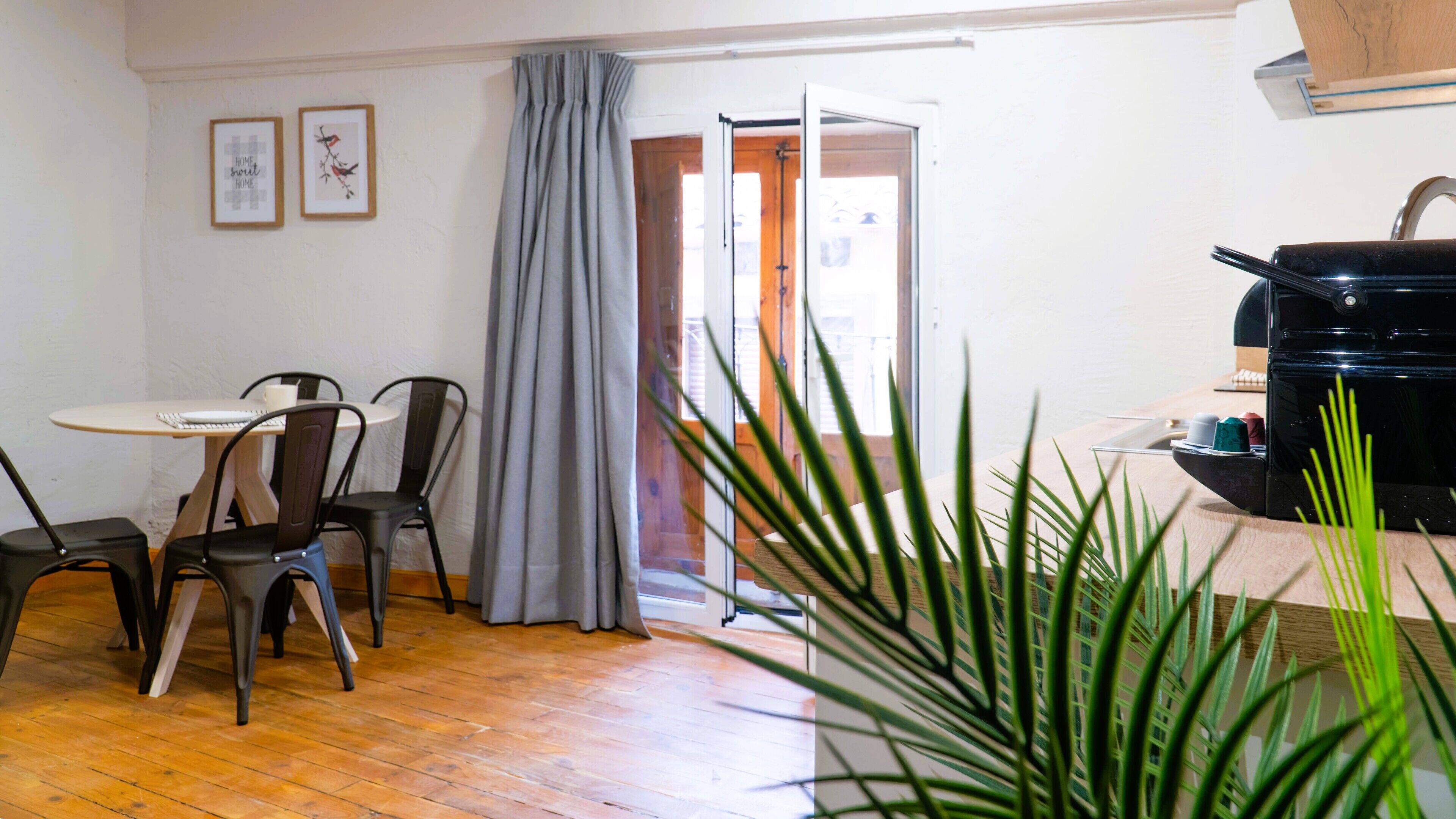 A room with a wooden floor, a dining table with chairs, a coffee machine, and a door leading outside.