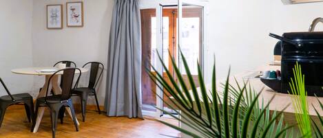 A room with a wooden floor, a dining table with chairs, a coffee machine, and a door leading outside.