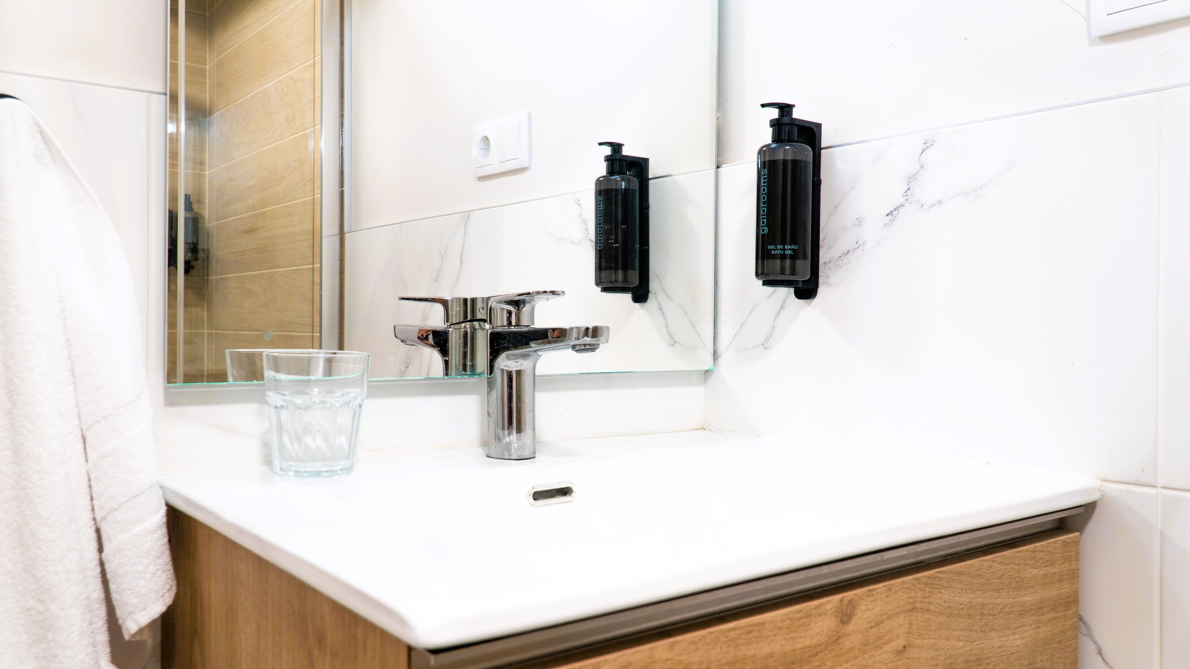 Un bagno moderno con un lavabo in marmo bianco, un rubinetto cromato, un bicchiere d'acqua e due erogatori di sapone neri.
