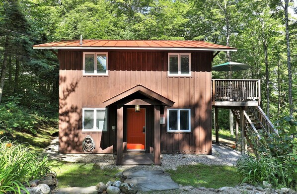 Une cabane en bois avec un toit rouge, un porche à l’avant et une terrasse dotée d’une balustrade.