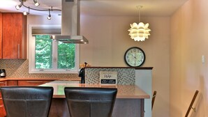 A modern kitchen with a large window, a clock, and a unique light fixture.