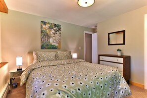 Une chambre à coucher comprenant un lit, une table de chevet, une lampe, une commode, un miroir et un tableau accroché au mur.