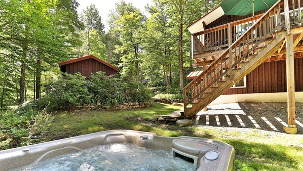 A hot tub in a lush garden with a wooden deck and stairs leading to a cabin.