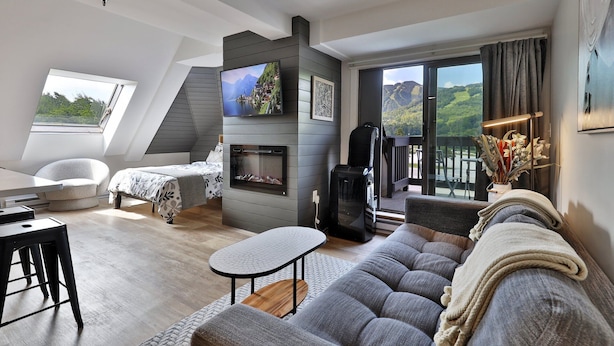 Un dormitorio tipo loft moderno con techo inclinado, chimenea, televisor grande y balcón con vistas panorámicas.
