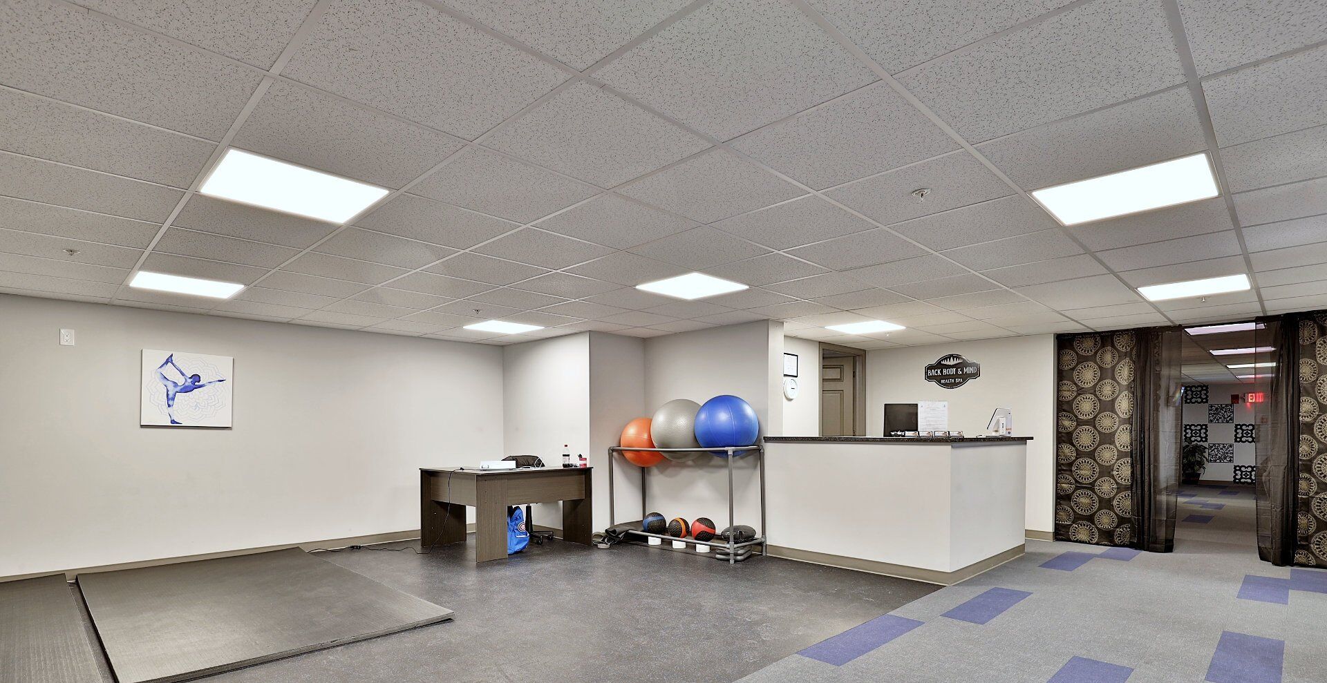A spacious room with a reception desk, a wall-mounted clock, and exercise balls.