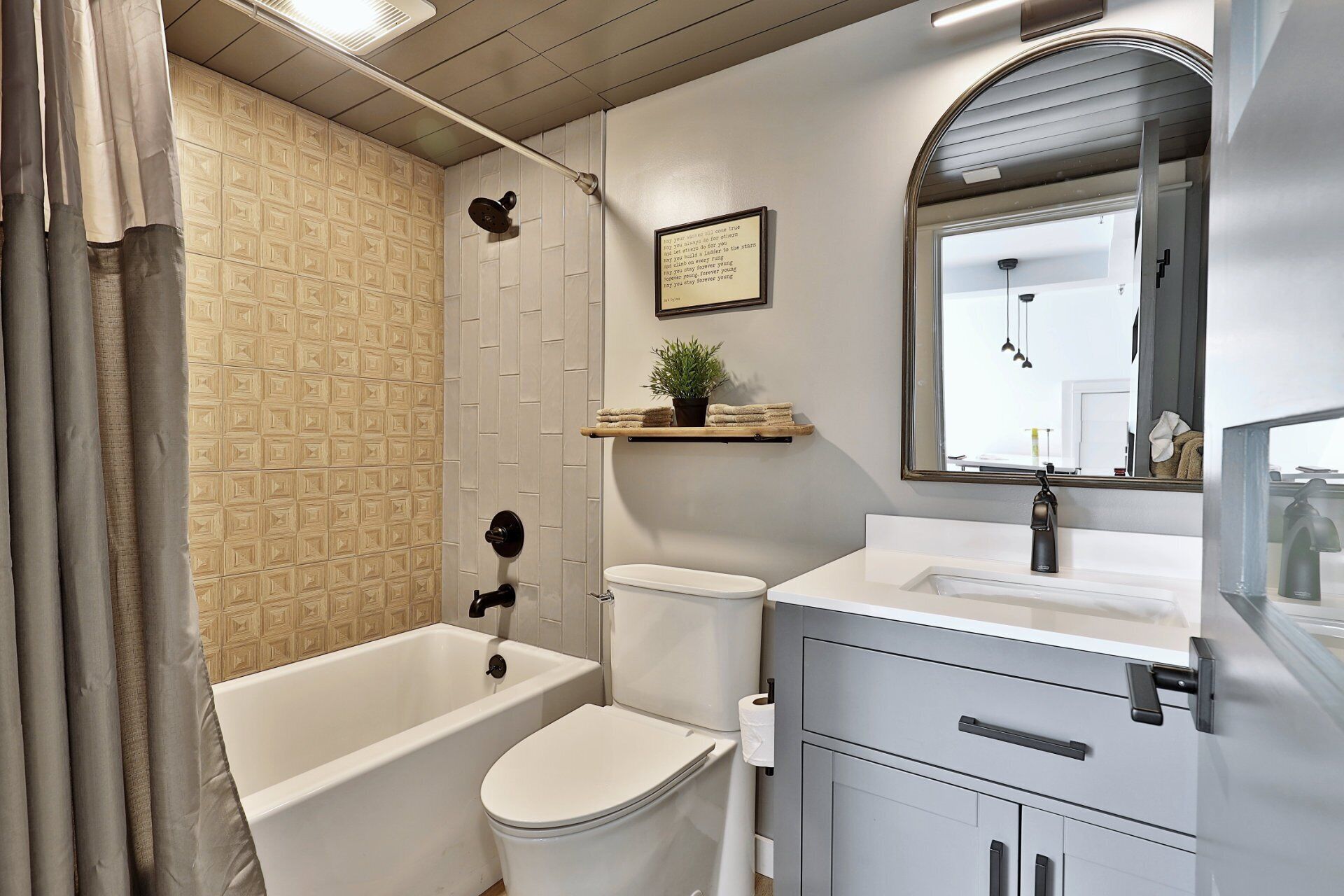 Un bagno con vasca, WC e lavandino. È presente un soffione doccia, un portasciugamani e una citazione incorniciata al muro.