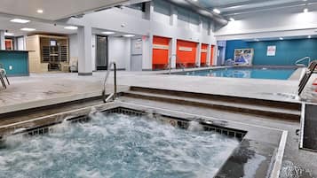 Una piscina cubierta con un jacuzzi, escalones que bajan a la piscina y un área de recepción con sillas.