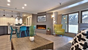 A modern living room with a fireplace, a dining area with blue chairs, and a sofa with a patterned throw. - Renovated. Mountain Views. Steps to Killington. Discounted Ski Rentals. 3C16 (Killington)