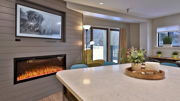 A modern living room with a fireplace, a large window, and a dining area. - Renovated. Mountain Views. Steps to Killington. Discounted Ski Rentals. 3C16 (Killington)