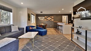 A modern living room with a sofa, a blue armchair, a coffee table, and a dining area with a bar.