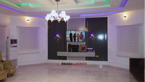 Un vaste salon agrémenté d’un lustre moderne, d’un téléviseur à écran plat fixé sur un mur à rayures noires et blanches, et d’un meuble de rangement minimaliste pour les appareils multimédias.