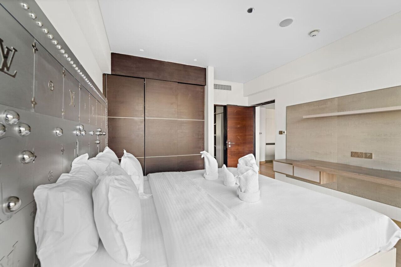 A modern hotel room with a large bed, a wardrobe with a mirror, and a seating area with a TV.