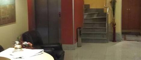 Un hall de hotel con mostrador de recepción, una escalera y una puerta que da a otra habitación.