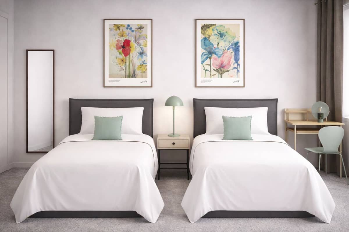 Habitación de hotel con dos camas, un escritorio, una silla y dos cuadros con motivos florales en la pared.