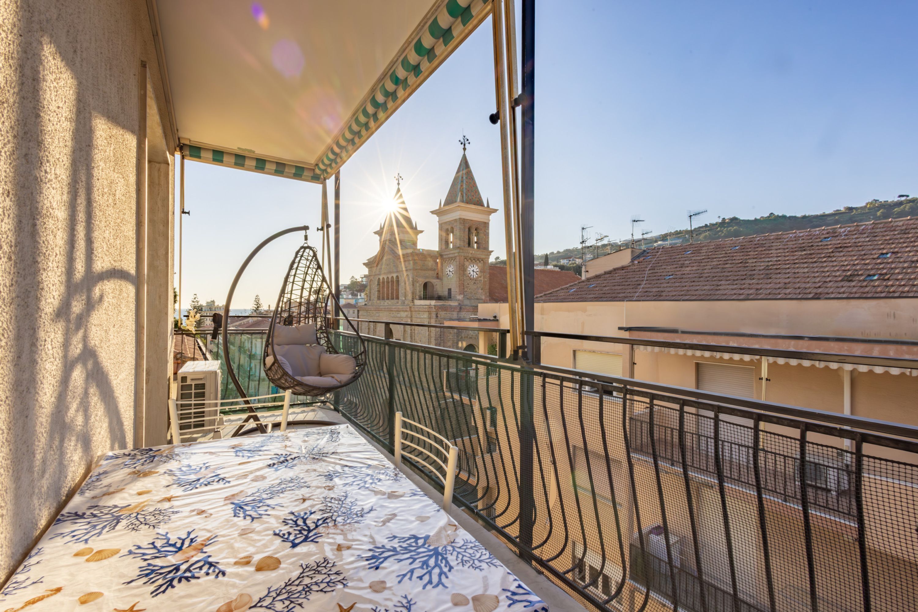 Ein Balkon mit Blick auf eine Kirche und Gebäude, einem Hängesessel und einer gemusterten Tischdecke.