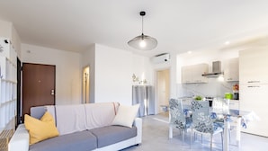 Un salon moderne comprenant un canapé, une table à manger et des chaises. Il y a également un coin cuisine avec des placards et une cuisinière.