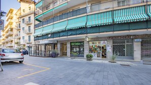 Une vue de rue avec une rangée de boutiques, dont une dont la devanture est visible et sur laquelle on peut lire l’inscription « PESCHERIA ».