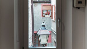 Vista attraverso una finestra di una porta su una strada, con cornice rossa e un vaso di fiori sul davanzale.