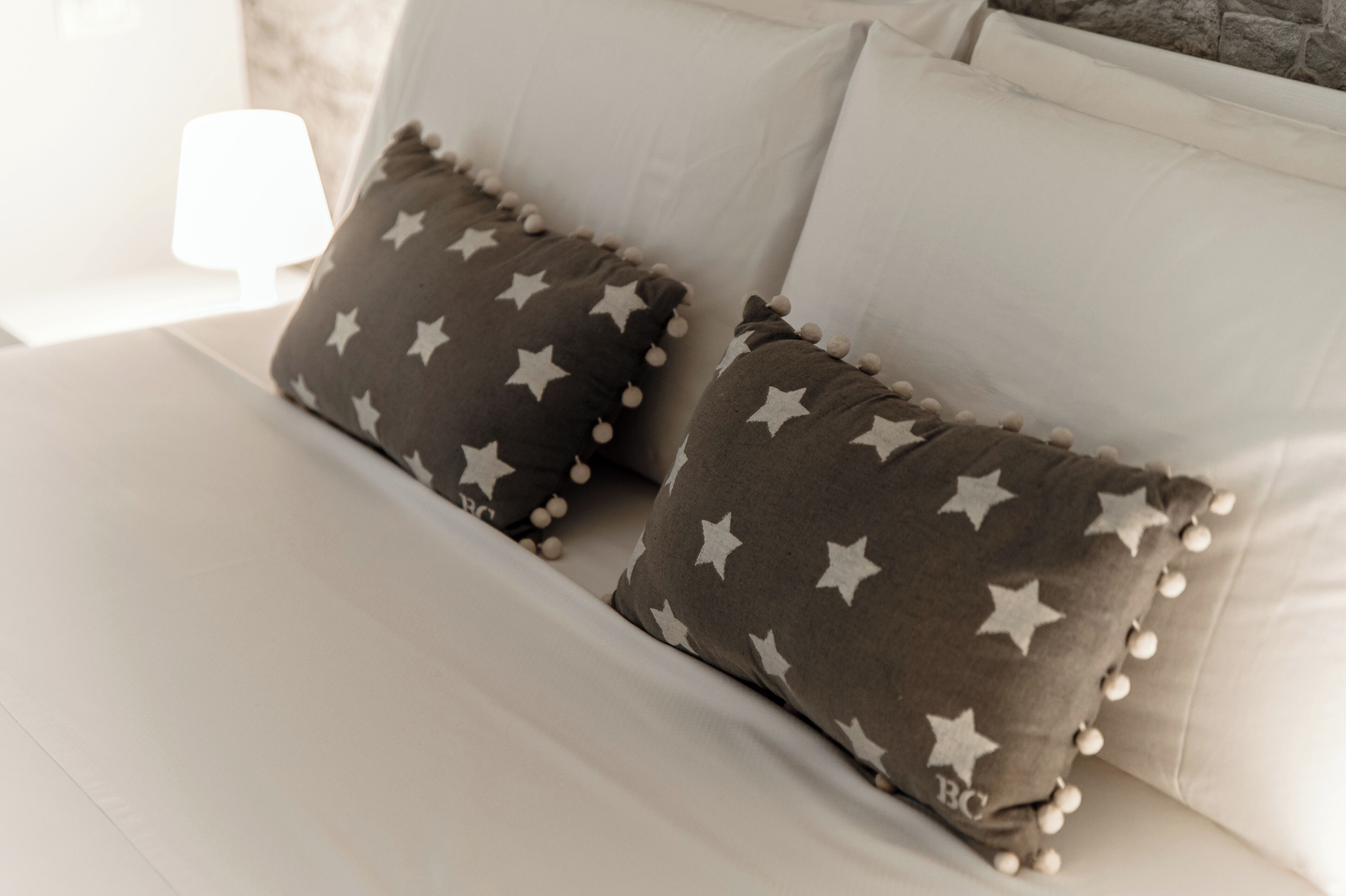 Una cama con sábanas blancas y dos almohadas con motivos de estrellas y borlas.