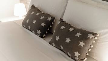 Una cama con sábanas blancas y dos almohadas con motivos de estrellas y borlas.