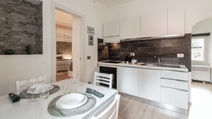 Una cucina moderna con mobili bianchi, una schiena di fiamma scura e un'area pranzo con un tavolo bianco imbandito per due.