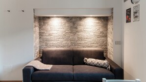 Un soggiorno moderno con una parete in pietra a contrasto, un divano marrone scuro e cuscini decorativi.