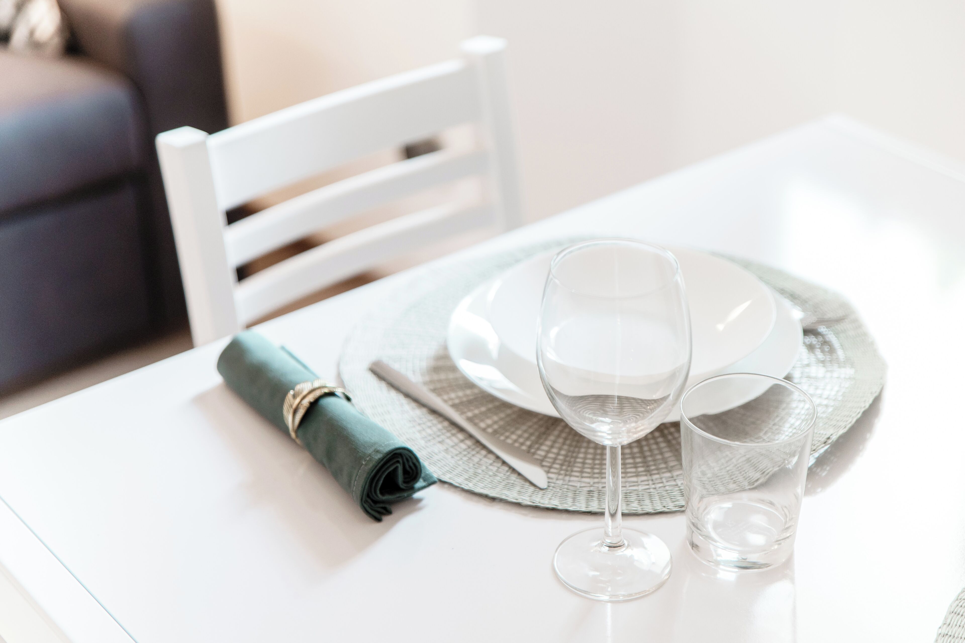 A dining table with a white plate, a wine glass, and a rolled napkin.